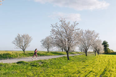 Frau läuft auf Fußweg inmitten von Mandelblüten in der Nähe von Wiese - EGHF00888