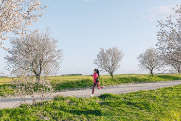 Frau joggt auf einem Fußweg in der Nähe einer Wiese - EGHF00889