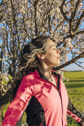Sorglose Frau mit geschlossenen Augen in der Nähe von Mandelblütenbäumen an einem sonnigen Tag - EGHF00892