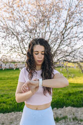 Frau, die vor einem Mandelblütenbaum steht und ihr Smartphone überprüft - EGHF00896