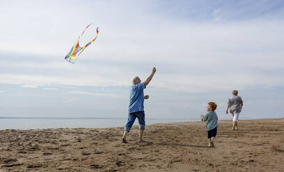 Grandparents spending leisure time and flying kite with grandson at beach - MBLF00291