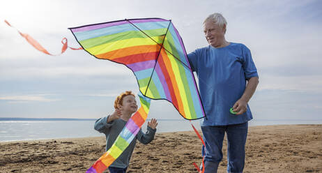 Älterer Mann bringt seinem Enkel am Strand das Drachensteigen bei - MBLF00293