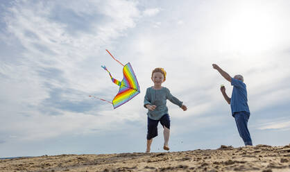 Verspielter Junge mit Großvater lässt am Strand einen Drachen steigen - MBLF00298
