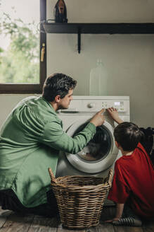Father and son operating washing machine in utility room at home - VSNF01755