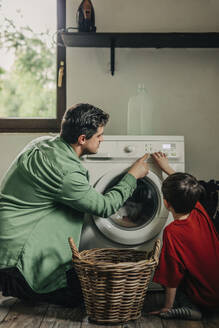 Vater und Sohn bedienen die Waschmaschine in der Waschküche zu Hause - VSNF01755