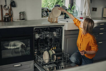 Frau stapelt gewaschene Teller auf der Küchentheke zu Hause - VSNF01766