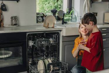 Lächelnde Frau mit Sohn in der Nähe der Spülmaschine in der Küche zu Hause - VSNF01767