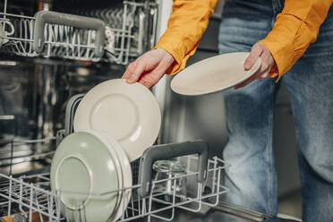Woman unloading washed plates from dishwasher at home - VSNF01773