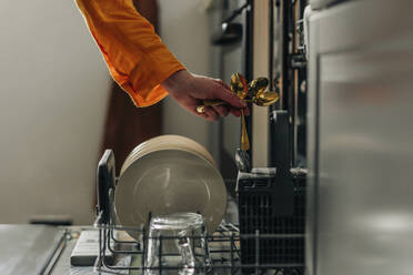 Woman picking up washed spoons from dishwasher at home - VSNF01775