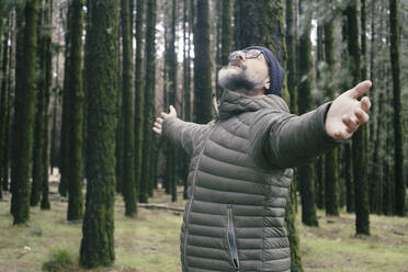 Man with arms outstretched amidst trees in forest - SIPF02896