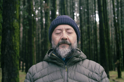 Mann mit geschlossenen Augen inmitten von Bäumen im Wald - SIPF02898