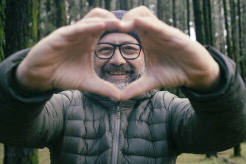 Lächelnder Mann mit herzförmiger Geste im Wald - SIPF02901
