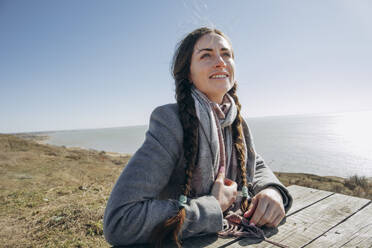 Nachdenkliche Frau sitzt auf einer Bank in der Nähe des Meeres an einem sonnigen Tag - KVBF00051