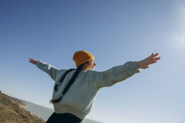 Happy woman standing with arms outstretched under clear sky - KVBF00054