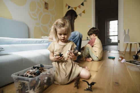 Blondes Mädchen spielt mit Spielzeug vor Mutter und Bruder zu Hause - KVBF00061
