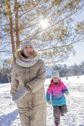 Mutter und Tochter laufen im Winterwald an einem sonnigen Tag - MBLF00299