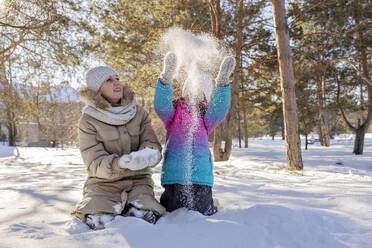 Mädchen wirft Schnee in der Nähe der Mutter im Winterwald - MBLF00301
