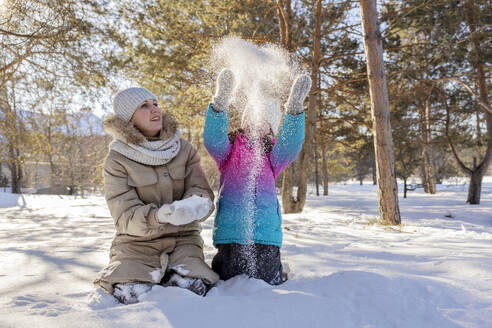 Girl throwing snow near mother in winter forest - MBLF00301