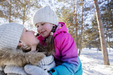 Smiling girl embracing mother in winter forest - MBLF00302