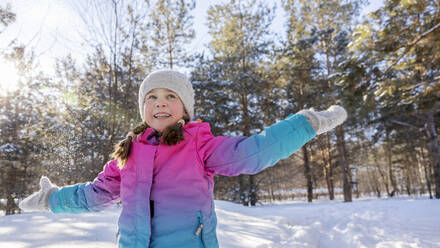 Carefree girl playing with arms outstretched in winter forest - MBLF00306