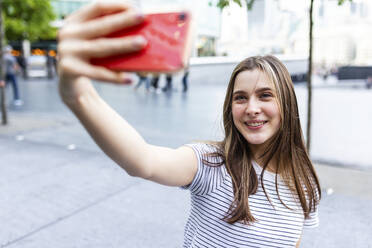 Smiling young woman taking selfie with smart phone at footpath - WPEF08658