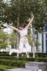 Cheerful young woman jumping in front of trees - WPEF08663