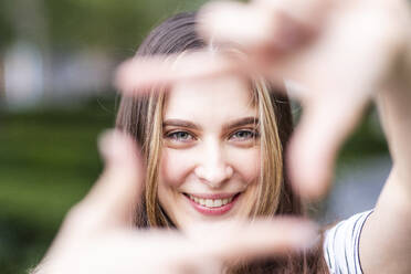 Smiling young woman looking through finger frame - WPEF08667