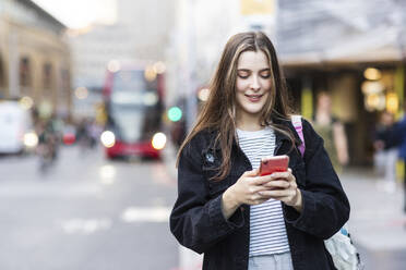 Glückliche junge Frau benutzt Smartphone in der Stadt - WPEF08677