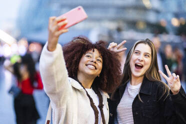 Cheerful woman taking selfie with friend gesturing peace sign - WPEF08682