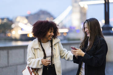 Happy woman enjoying with friend holding smart phone in London City - WPEF08683