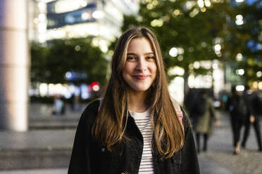 Smiling young woman in city at night - WPEF08695