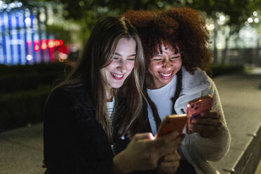 Glückliche junge Freunde, die nachts ihr Smartphone benutzen - WPEF08704