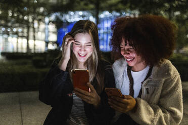Happy friends using smart phones in city at night - WPEF08706