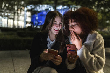 Happy friends sharing smart phones at night - WPEF08707