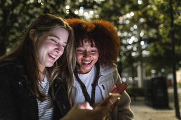 Smiling friends sharing smart phones at night - WPEF08709