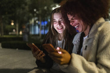 Cheerful young friends using mobile phones at night - WPEF08710