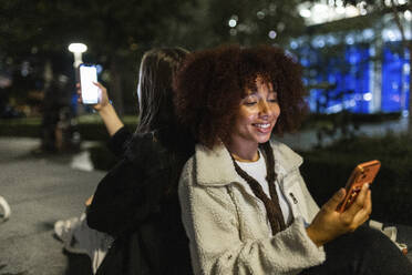 Smiling young friends using smart phones at night - WPEF08714