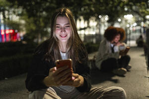 Smiling beautiful woman using mobile phone at night - WPEF08719