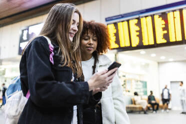 Smiling woman with friend using smart phone at railroad station - WPEF08737