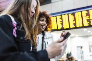 Happy woman with friend using smart phone at railroad station - WPEF08738