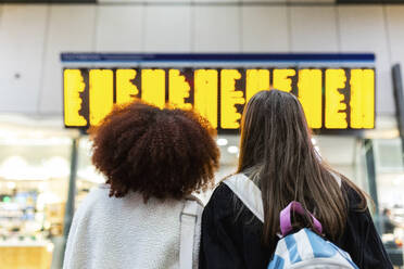 Friends looking at arrival departure board at railroad station lobby - WPEF08741