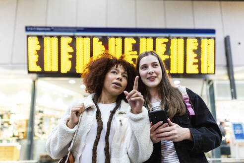 Woman gesturing with friend standing at railroad station - WPEF08743