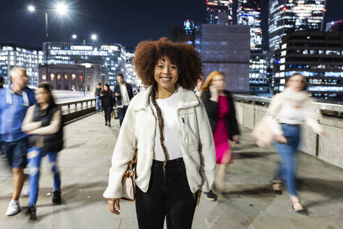 Happy young woman standing in City of London at night - WPEF08744