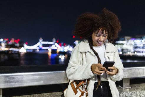 Glückliche junge Frau, die in der Londoner City nachts ihr Smartphone benutzt - WPEF08745