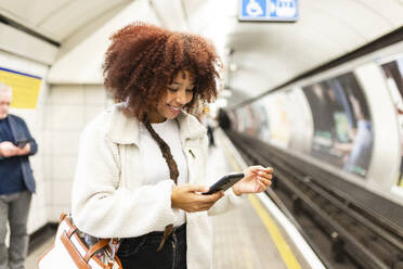 Lächelnde Frau mit Mobiltelefon in der U-Bahn - WPEF08747