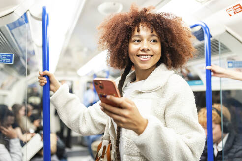 Lächelnde Frau mit Smartphone im U-Bahn-Zug stehend - WPEF08748