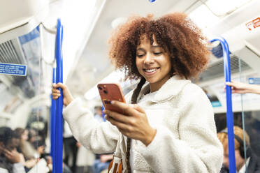 Smiling woman using smart phone in subway train - WPEF08749