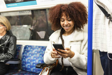 Smiling young woman sitting and using smart phone in subway train - WPEF08751