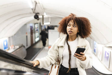 Woman standing with mobile phone on subway escalator - WPEF08752
