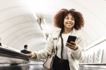 Happy woman with mobile phone on subway escalator - WPEF08754